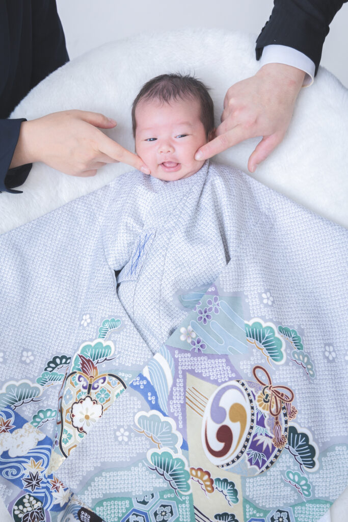 水色の疋田の産着を着てパパとママにほっぺを触られている赤ちゃん